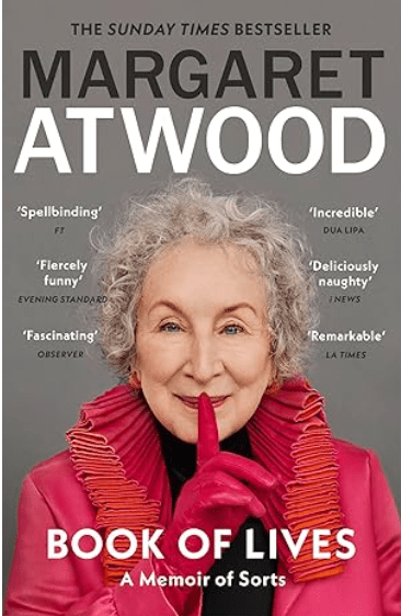 An image of Margaret Atwood's autobiography, Book of Lives. A grey background with black and white text.  picture of Margaret takes up the majority of the space. She is dressed in a fabulous red and pink jacket with a very flamboyant collar, is wearing a black rollneck under and has a fuchsia pink glove. She is holding her right hand up to her face with her finger over her lips. 